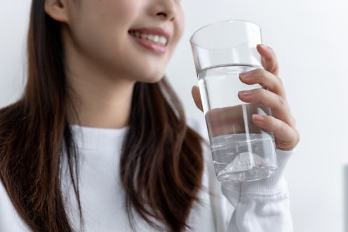 young pretty Asian girl sitting on a cozy sofa in the living room while drinking water.