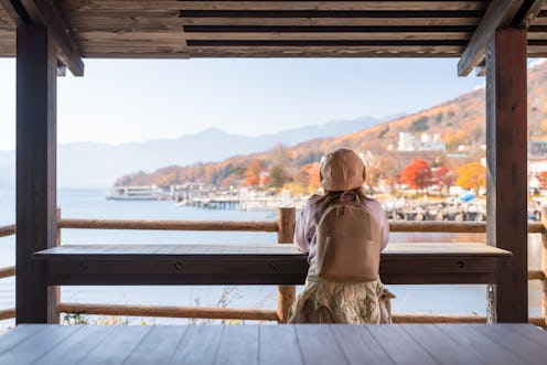 Rear view of a woman sitting looking at a beautiful lake Chuzenji while travelling at Nikko National...