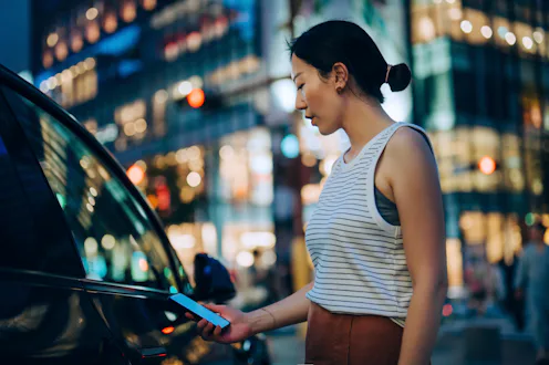 Young Asian woman using mobile app device on smartphone to unlock the doors of her intelligence car ...