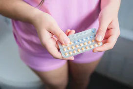Top View of Unidentified Young Woman, Dressed in a Pink Pajama, holding her Contraceptive Pills, Whi...