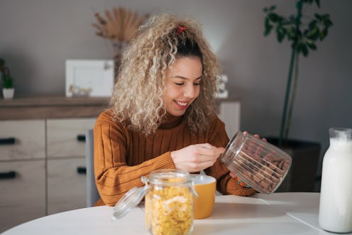 A young woman with curly hair is preparing a healthy breakfast. There is cereal with milk.
