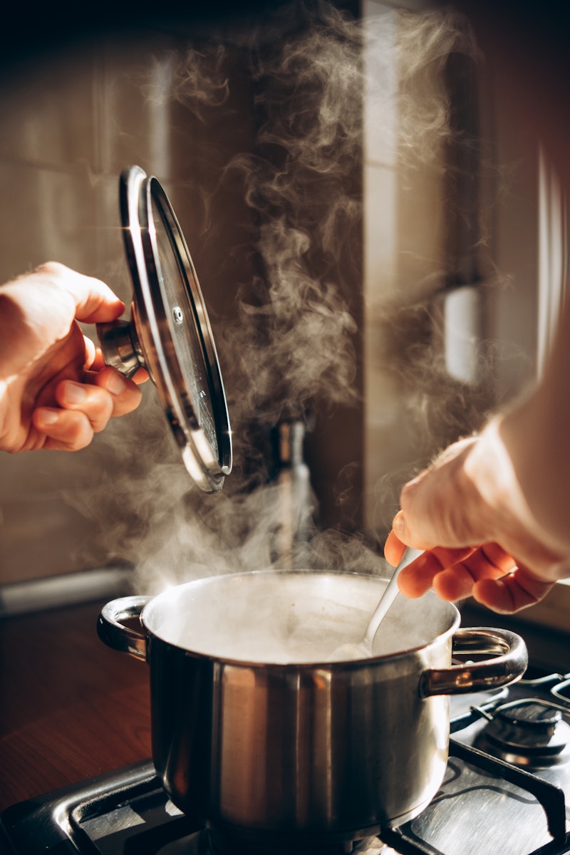 a man cooks in the kitchen cooks food in a pot and stirs with a spoon
Steam comes out of the pot