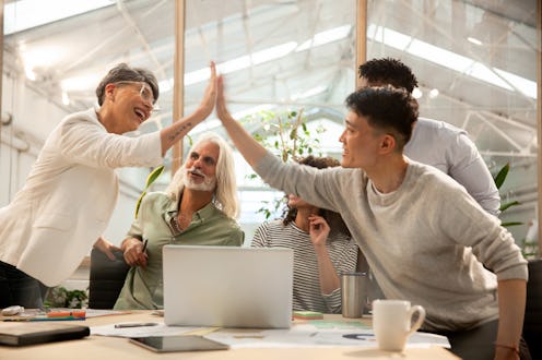 Side view of agency workers high fiving during meeting at office