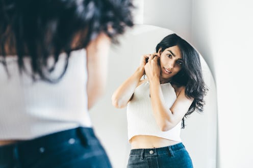 A woman puts on earrings and looks in the mirror at home.