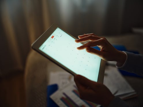 Close up of unrecognizable businesswoman working on digital tablet in a dark room. Photographed in m...