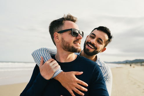 Affectionate young gay couple standing arm in arm together on a sandy beach by the ocean in summer