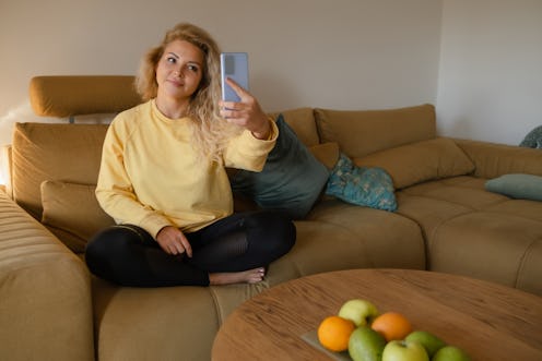 Happy woman making video call via smartphone while sitting on sofa at home