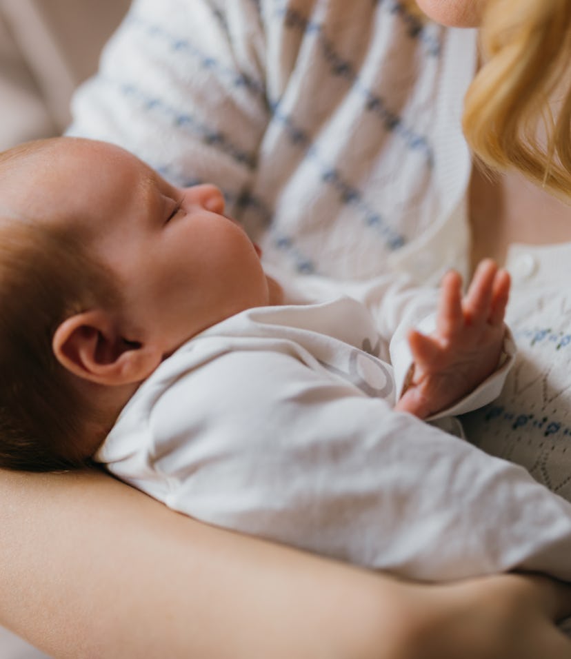 An unrecognizable blonde Caucasian woman is looking at her cute baby while holding it. Her unrecogni...