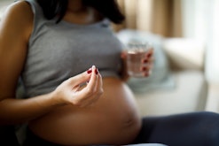Pregnant woman taking pill at home, in a story about whether it's safe to take tylenol while you're ...