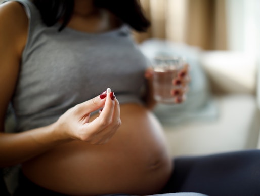 Pregnant woman taking pill at home, in a story about whether it's safe to take tylenol while you're ...
