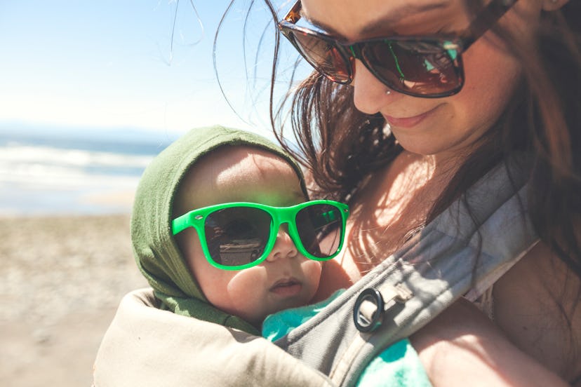 Mother holding baby son at beach and both are wearing sunglasses