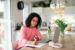 Young multiracial woman with black curly hair having home office in kitchen, writing notes.