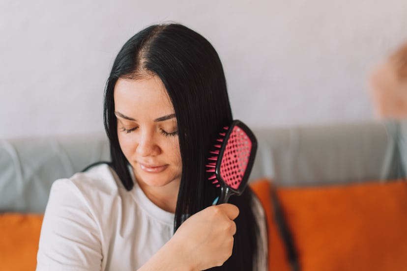 Lady with black hair combing her hair while sitting on the couch.