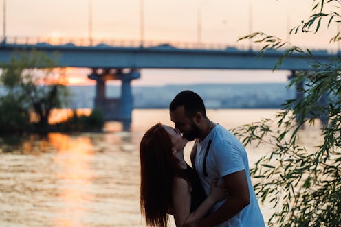 Sunset kiss: Amidst serene beauty of riverside sunset, loving young couple lips meet in tender kiss,...