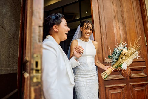 A radiant couple in wedding attire laugh and hold hands exiting  a city building, their joy palpable...