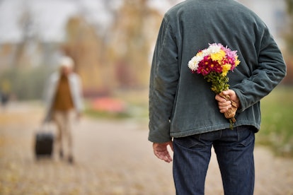 Back view of a senior man hiding flower bouquet while waiting for his wife's arrival from a trip in ...