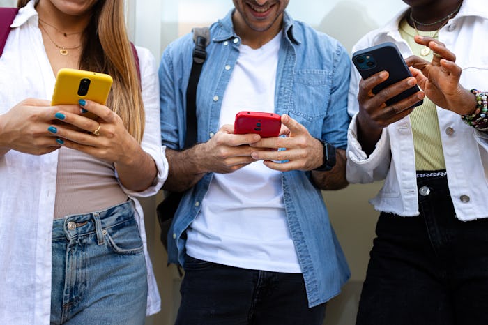 Close up of unrecognizable multiracial teenage college student friends using smart phone ignoring ea...