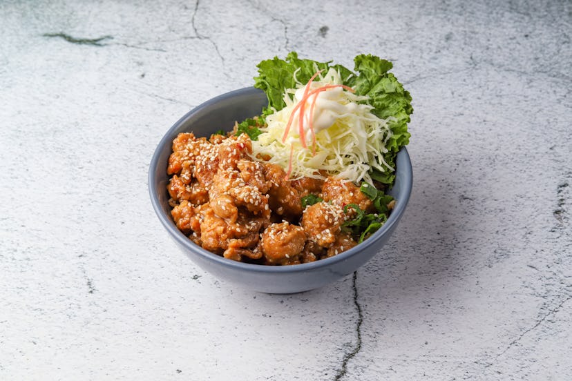 Orange chicken with salad in a bowl on white marble background.