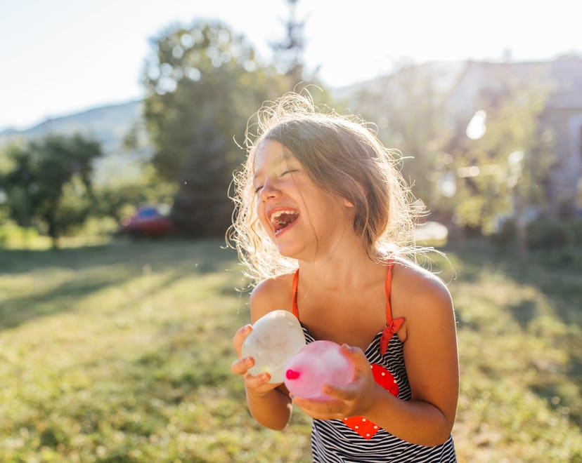 Water balloon games for kids. Smiling girl holding colorful balls filled with water. Cheerful and re...