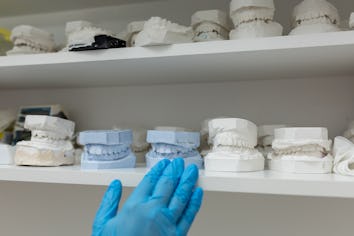 In contemporary dental clinic unrecognizable dentist gloved hands gently arranging dental molds on s...