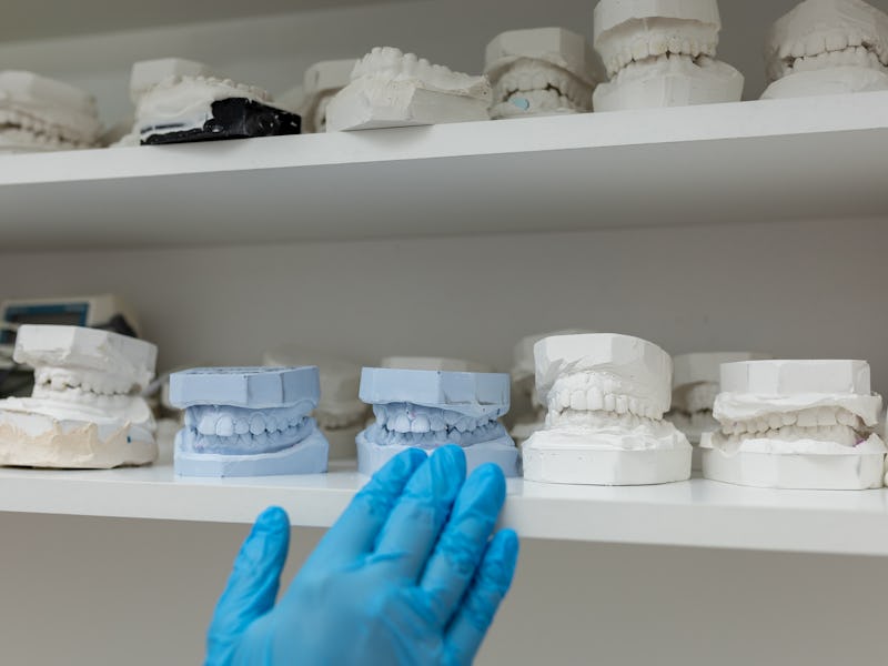 In contemporary dental clinic unrecognizable dentist gloved hands gently arranging dental molds on s...