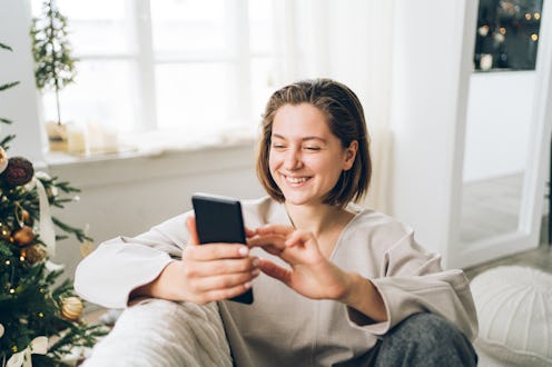 Laughing woman is talking on the video call sitting on sofa in light interior. Front view