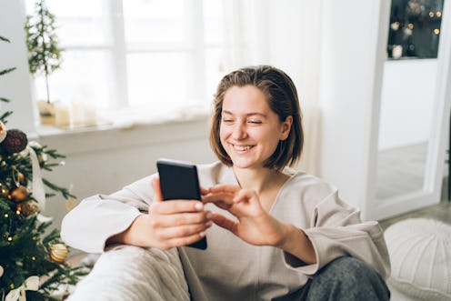 Laughing woman is talking on the video call sitting on sofa in light interior. Front view
