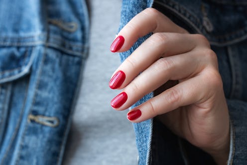 Female hand in denim jacket with beautiful manicure - red short gel nails. Nail care concept