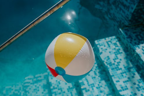 Simple background image of a multicoloured striped beach ball floating in an outdoor swimming pool. ...