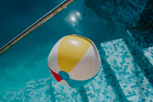 Simple background image of a multicoloured striped beach ball floating in an outdoor swimming pool. ...