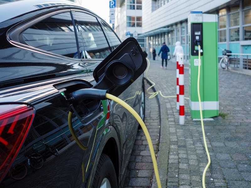 January 09, 2024: Selective focus, EV Electric Vehicle changing station on sidewalk beside car park ...