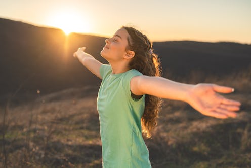 Happy teenage girl with closed eyes enjoying nature with open arms