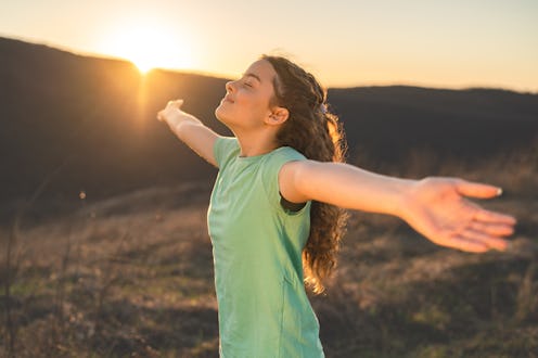 Happy teenage girl with closed eyes enjoying nature with open arms