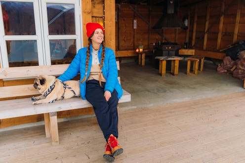 Front view of smiling female in blue jacket sitting with a dog in the gapahuk contemplating a view ...