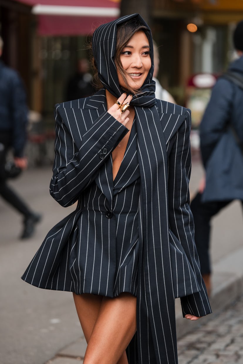 PARIS, FRANCE - MARCH 01: Ashley Park wears black striped blazer dress with matching long scarf, out...