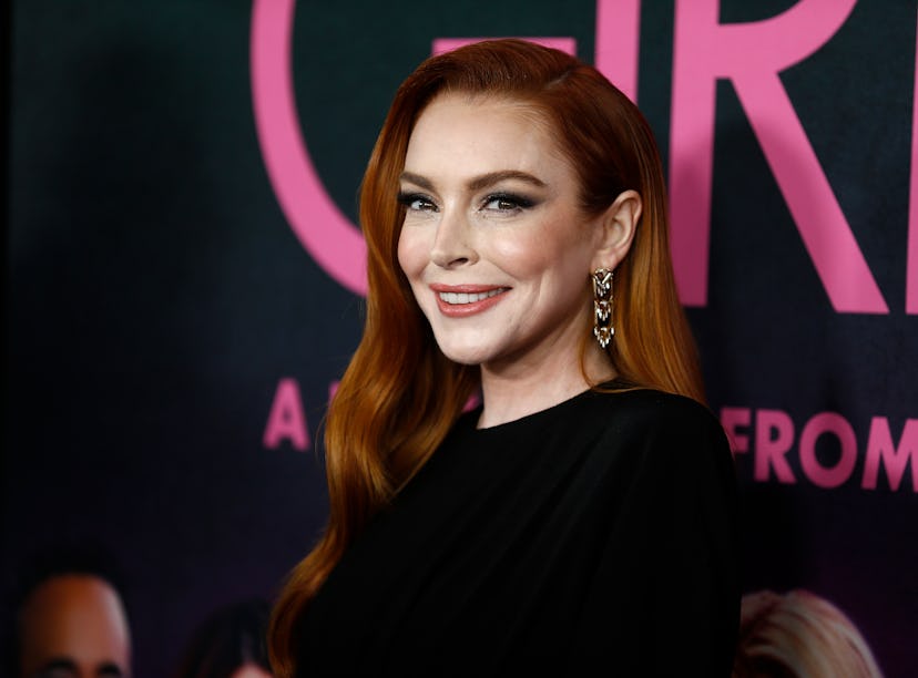 Woman with long red hair smiling at a movie premiere, wearing a black dress and elegant earrings, wi...