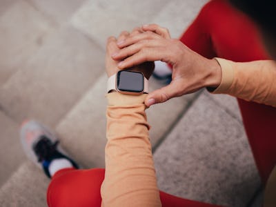Close-up of an athlete's hands adjusting a smartwatch while sitting and taking a break during an out...