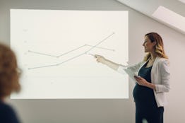 Smiling Pregnant Woman Holding digital tablet and giving presentation in office. Pointing to chart w...
