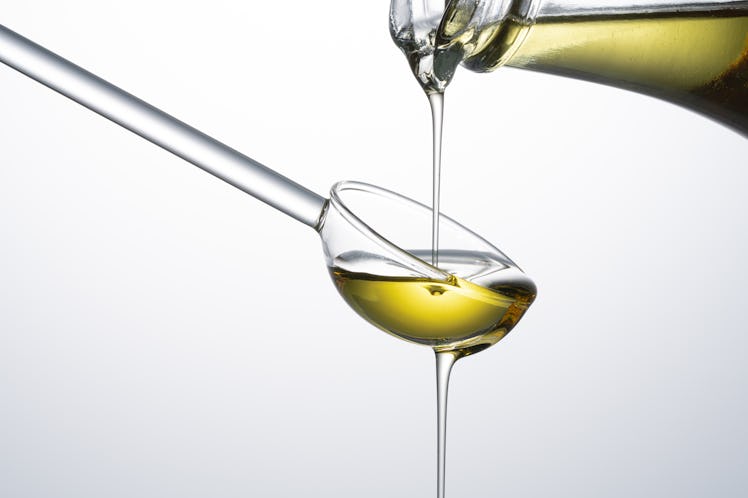 Olive Oil Pouring Into a Glass Spoon From Oil Bottle on White Background Close-up View.