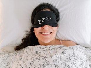 Top view of brunette woman smiling covered with white duvet relaxing of a good night sleep at home. ...