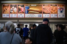 Customers wait in line to order below signage for the Costco Kirkland Signature $1.50 hot dog and so...