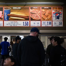 Customers wait in line to order below signage for the Costco Kirkland Signature $1.50 hot dog and so...