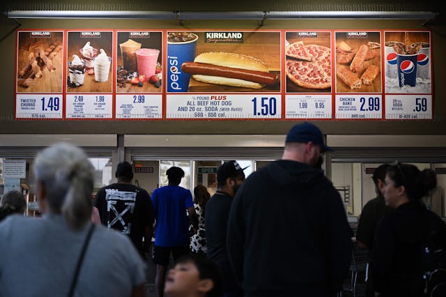 Customers wait in line to order below signage for the Costco Kirkland Signature $1.50 hot dog and so...