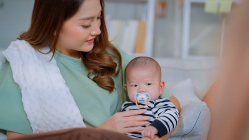 a woman bottle feeding her newborn baby at home asian mother sit on sofa feeding bottle of milk to h...
