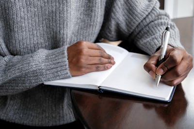 Close-up of unrecognizable black woman writing in journal at kitchen table