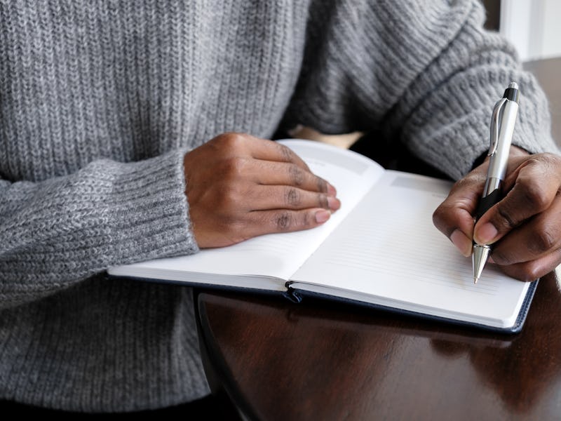 Close-up of unrecognizable black woman writing in journal at kitchen table