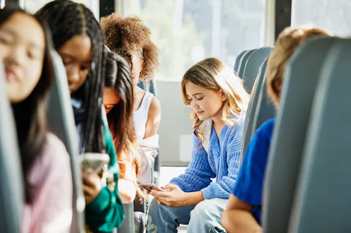 Medium wide shot of middle school girl looking at smart phone while commuting to school with friends...