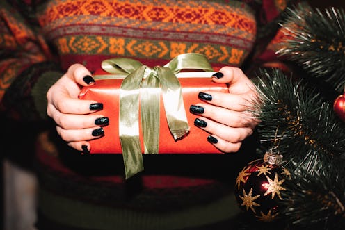 Young woman holding Christmas present standing by Christmas tree at home