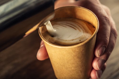 Barista pouring milk in cappuccino coffee in coffeeshop. Barista make coffee froth art on paper cup.