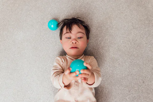 Directly above view of a young male toddler who has down syndrome lying on his back on the living ro...